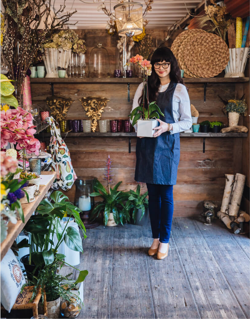 A flowershop keeper holding an orchid plant and smiling at the camera